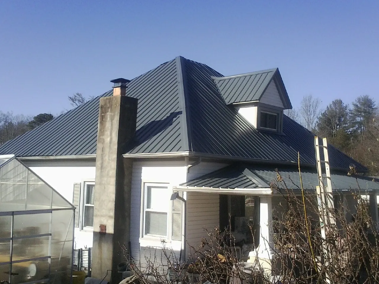 Dark blue standing seam metal roof on a white farmhouse with dormer — Slate & Tile Roof Repair by Roofing Brothers in Champlin