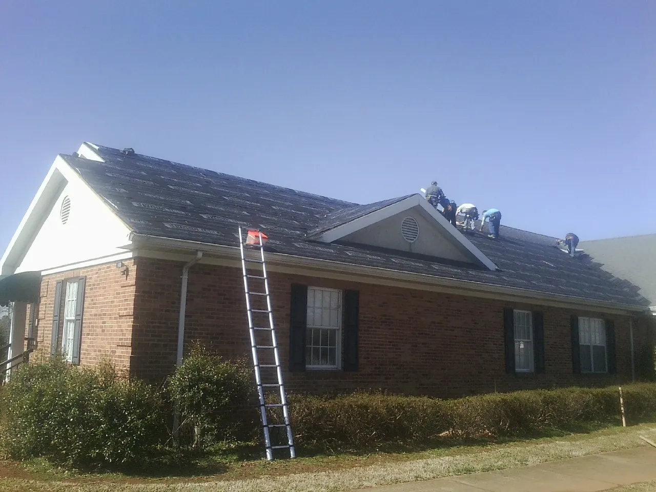 Crew tearing shingles off a brick ranch roof with a ladder set — Emergency Roof Repair work by our crew in Champlin