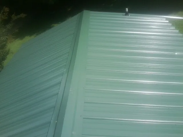 New green metal panels meeting at the ridge of a roof — Flat Roof Repair work by our crew in Champlin