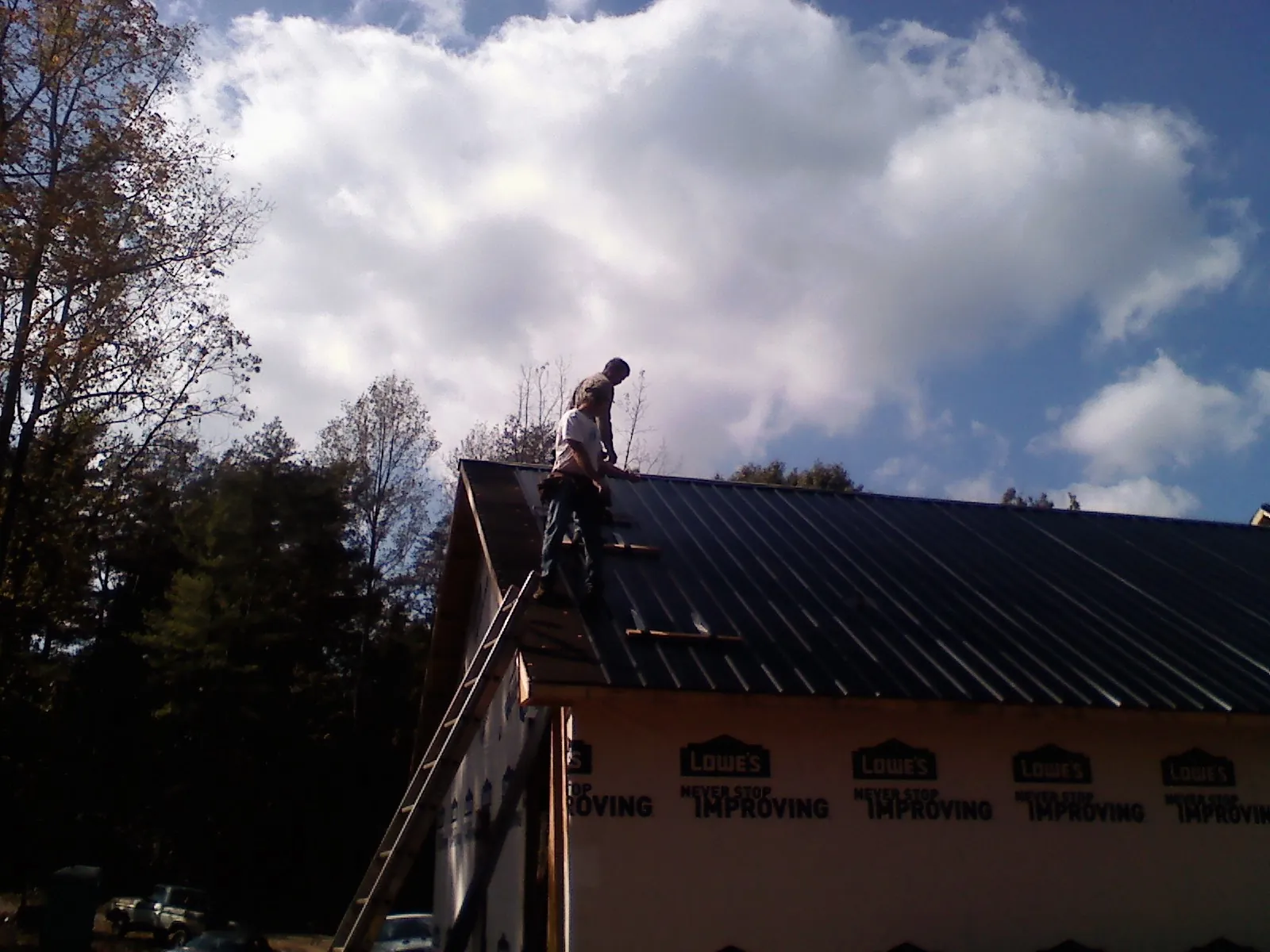 Roofer fastening dark metal panels high against a cloudy sky, from a Roof Inspection job in Champlin