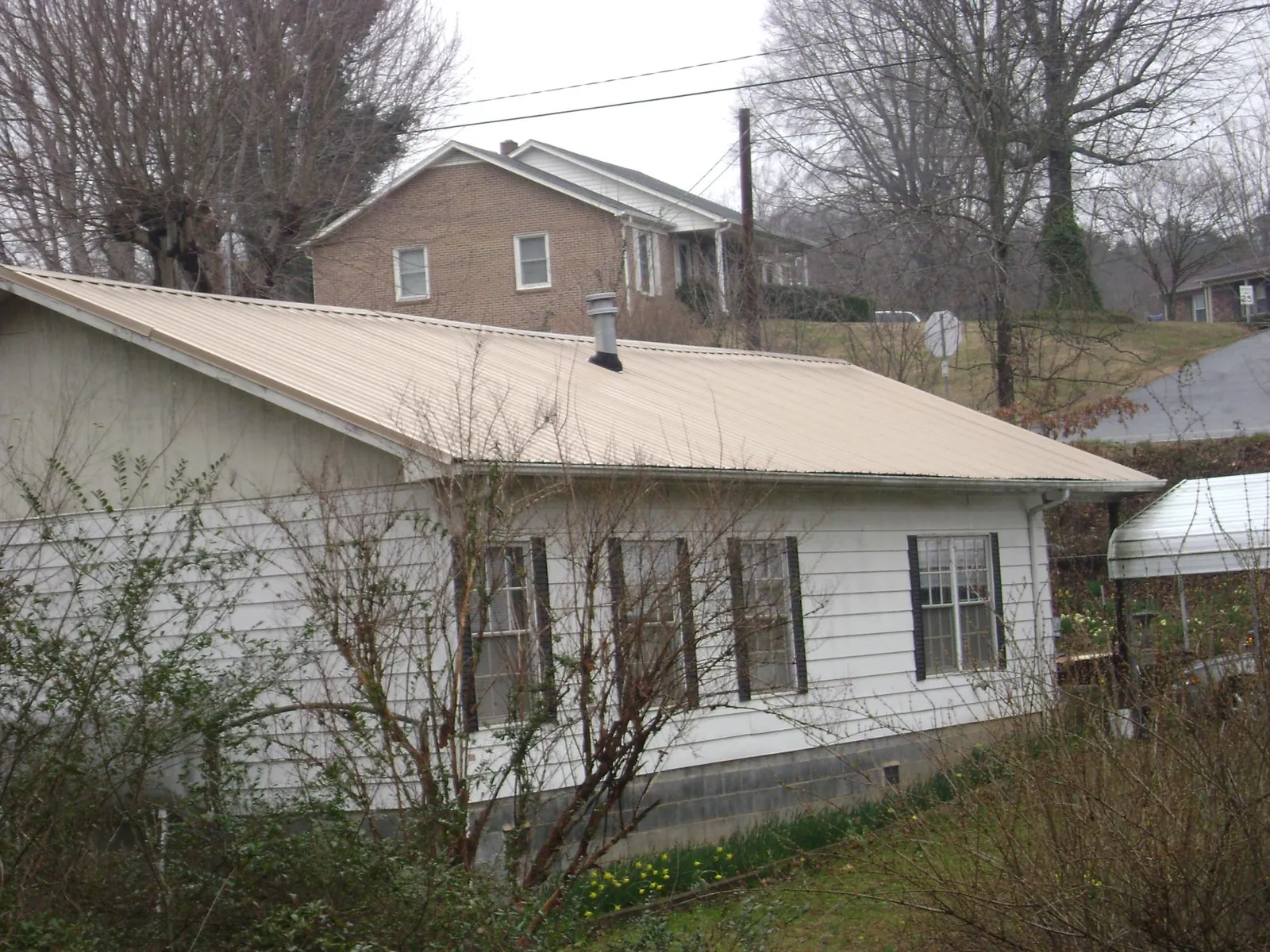 Tan metal roof on a white sided house set into a hillside — Commercial Roofing by Roofing Brothers in Champlin